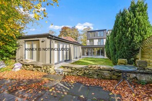 A modern two-story house with a stone facade, a glass conservatory, and a well-maintained garden with a stone wall and a small table. - Stylish 4BR Executive Home/Huge Kitchen/Sleeps7 (Bolton)