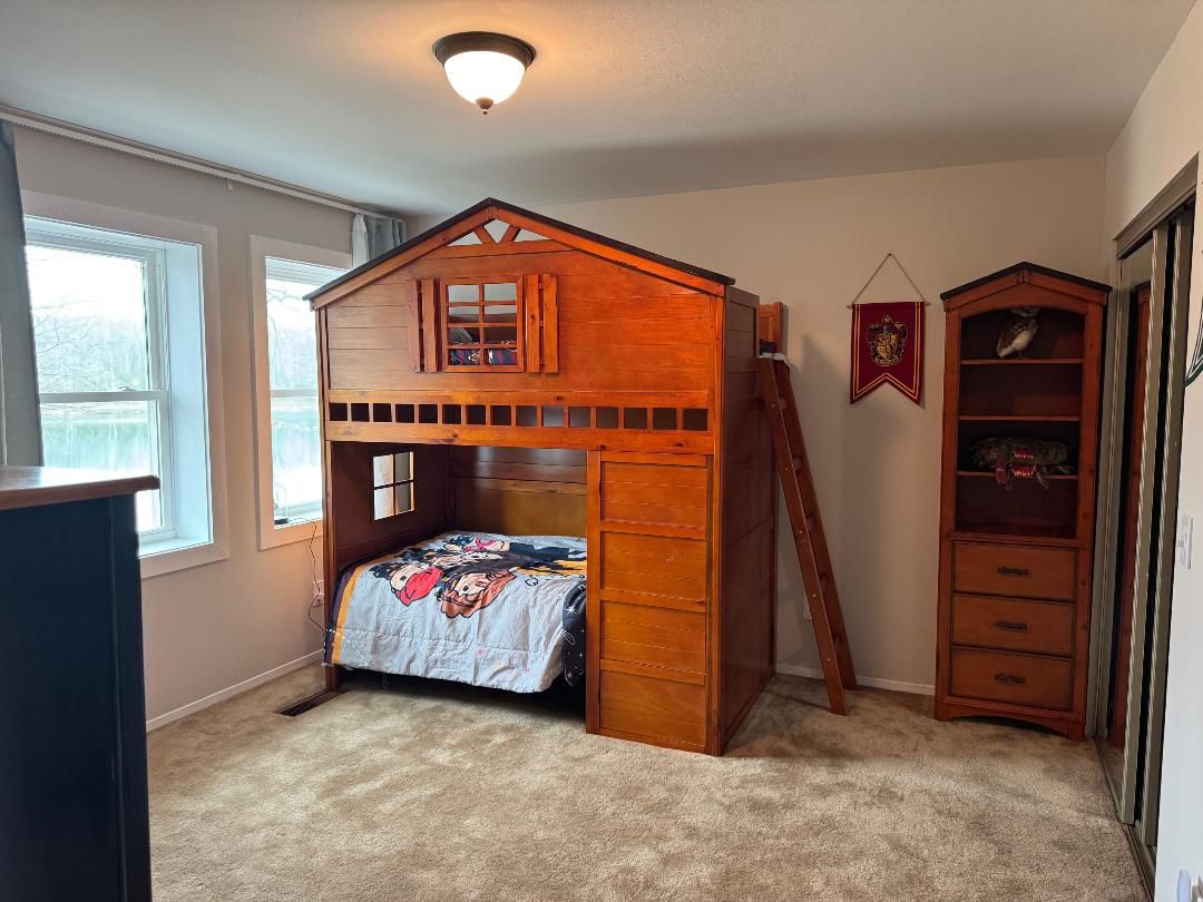 Un dormitorio con una cama nido de madera, un aparador, una escalera y una ventana.