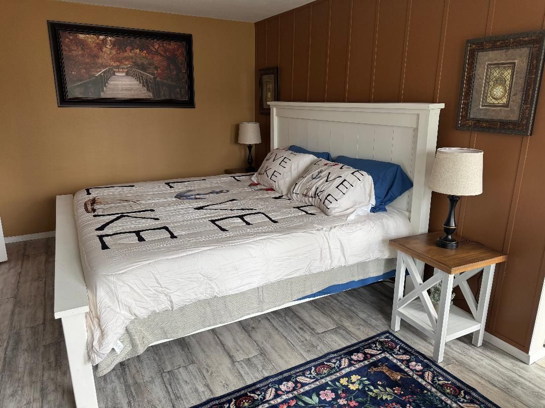A bed with a white headboard, a patterned bedspread, and a blue pillow. There is a small bedside table with a lamp and a decorative item on it.