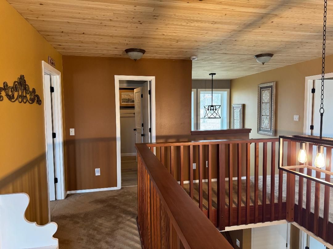 Un couloir avec un plafond en bois, une porte blanche et une rambarde en bois.