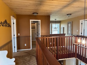 A hallway with a wooden ceiling, a white door, and a wooden railing. - Hickory Lake House  (Wright City)