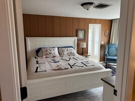 Un dormitorio con una cama blanca, una silla azul y una puerta que da a otra habitación.