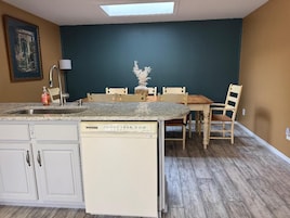 Una cocina con lavavajillas, una mesa de comedor con sillas e iluminación colgante.
