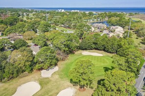 An aerial view of a golf course with sand bunkers, trees, and residential buildings in the background. - Harbour Point 806 (Miramar Beach)