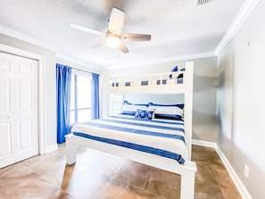 Ein Schlafzimmer mit einem Bett, einem Deckenventilator, einem Fenster mit Vorhängen und einer Tür.
