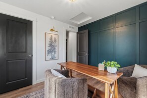 Ein Essbereich mit einem Holztisch und zwei gepolsterten Stühlen, einem gerahmten Kunstwerk an der Wand und einer Tür mit dunkler Oberfläche.