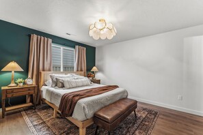 Ein Schlafzimmer mit Bett, Nachttischen, einer Bank, einem Teppich und einer Deckenleuchte.