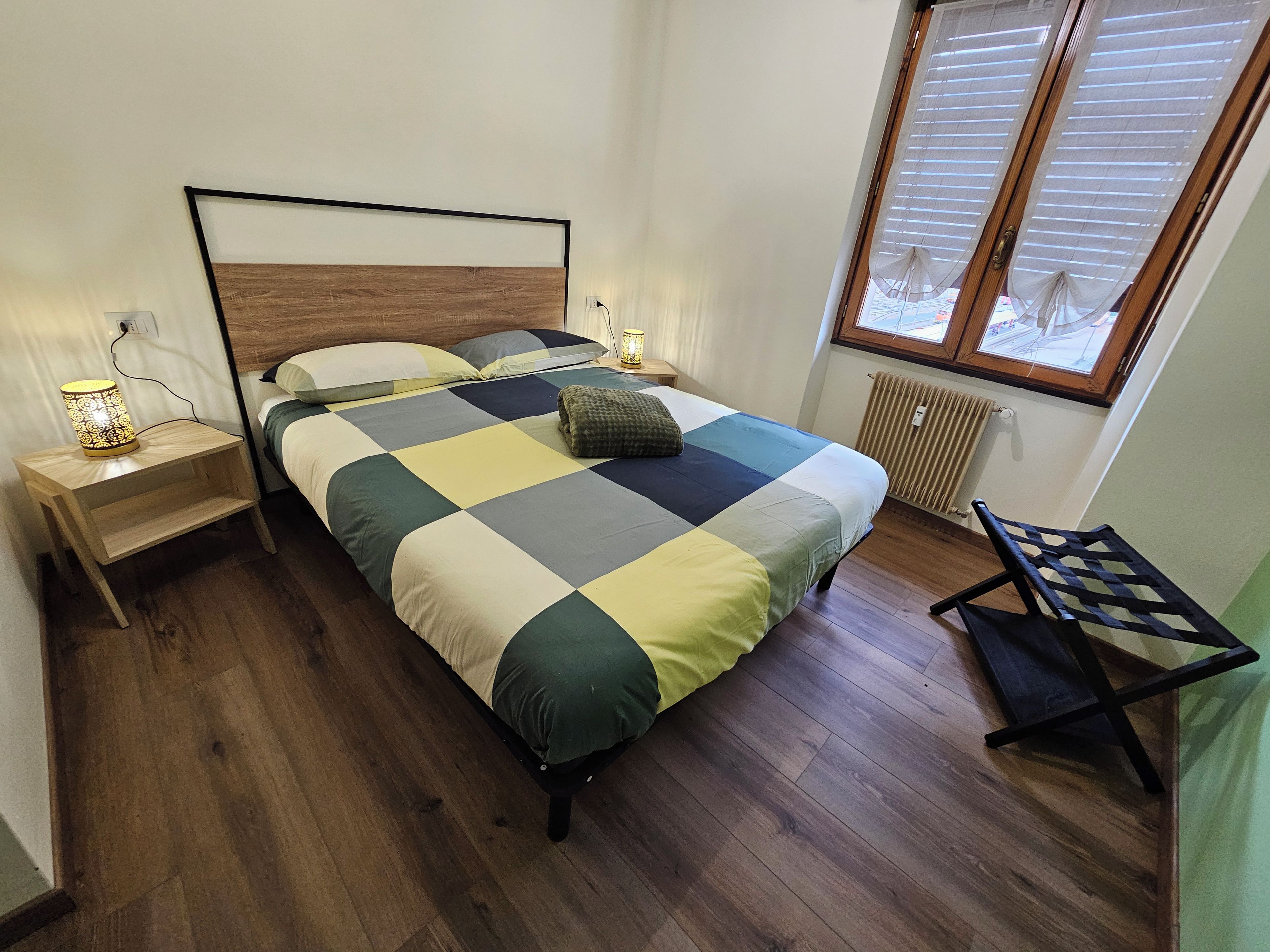 A bedroom with a bed, bedside tables, a lamp, a window with blinds, and a chair.