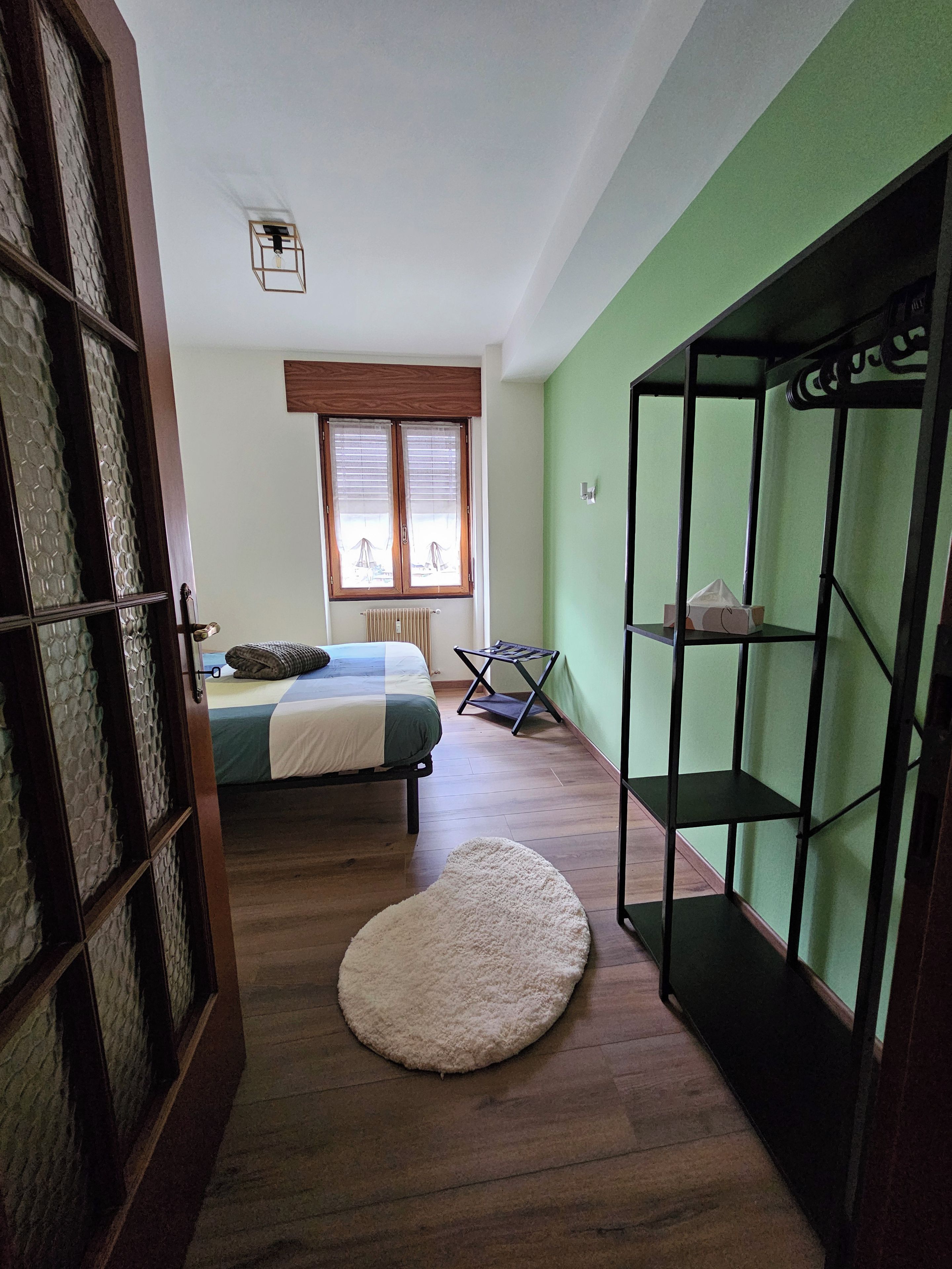 Un dormitorio con cama, radiador, ventana con persianas, suelo de madera y pared verde.