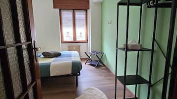 Un dormitorio con cama, radiador, ventana con persianas, suelo de madera y pared verde.