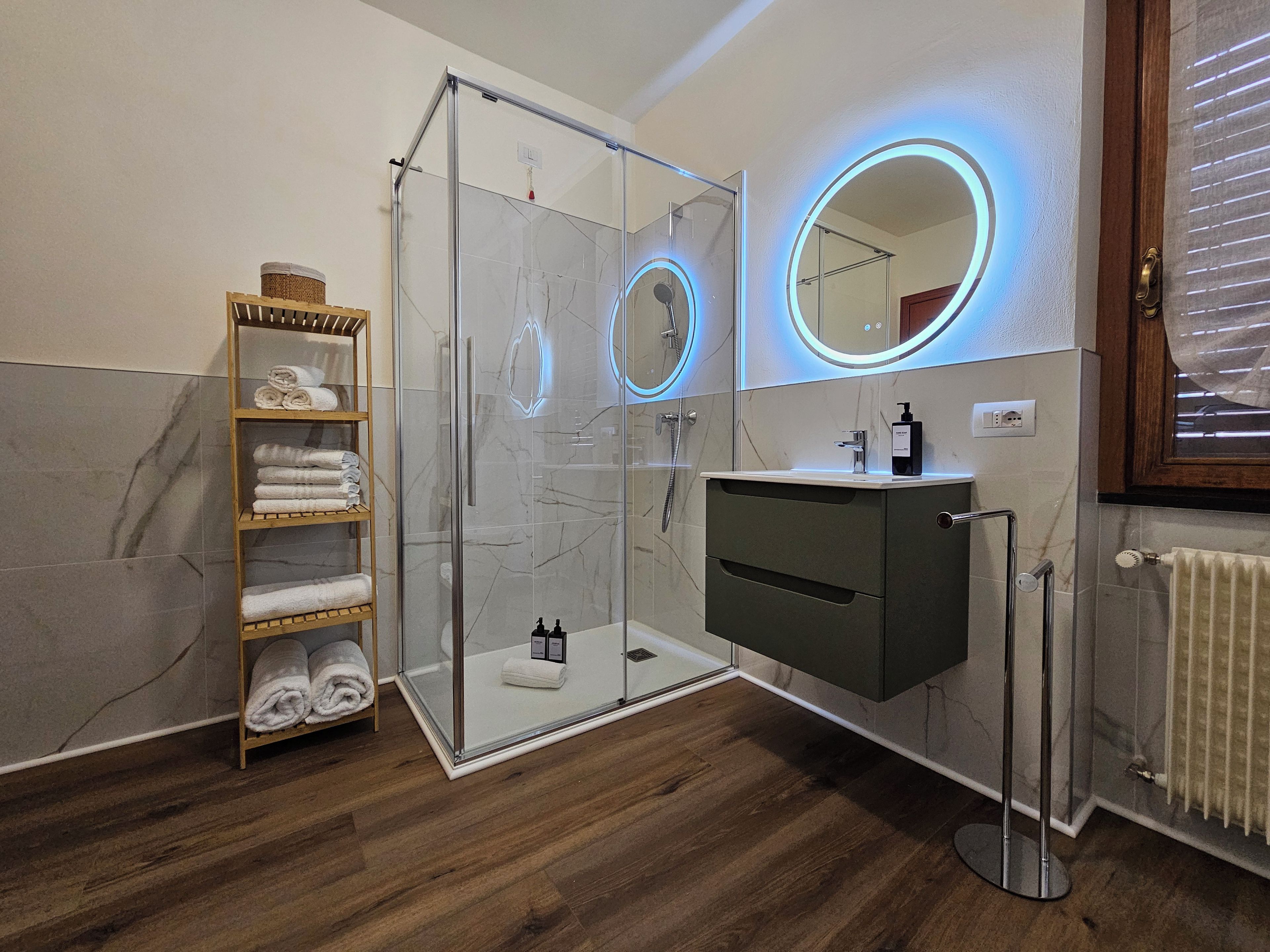 Ein modernes Badezimmer mit einer gläsernen Duschkabine, einem Waschtisch inklusive Spiegel und einem hölzernen Handtuchhalter.