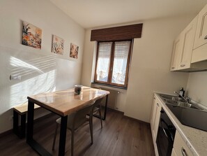 Een keuken met een houten tafel, een raam met zonwering en een radiator.