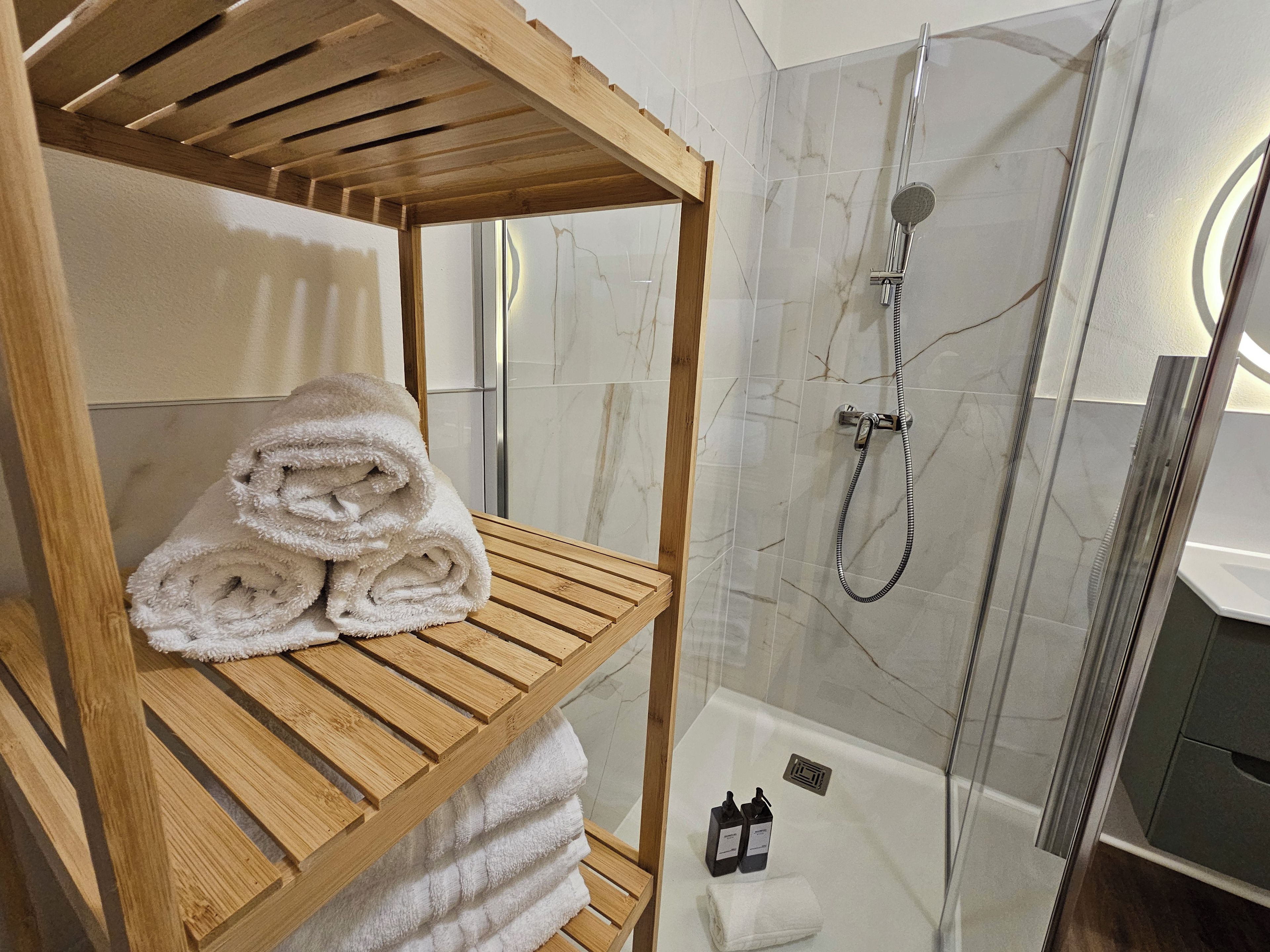 A bathroom with a wooden shelf holding rolled towels, a glass shower enclosure, and a white bathtub.