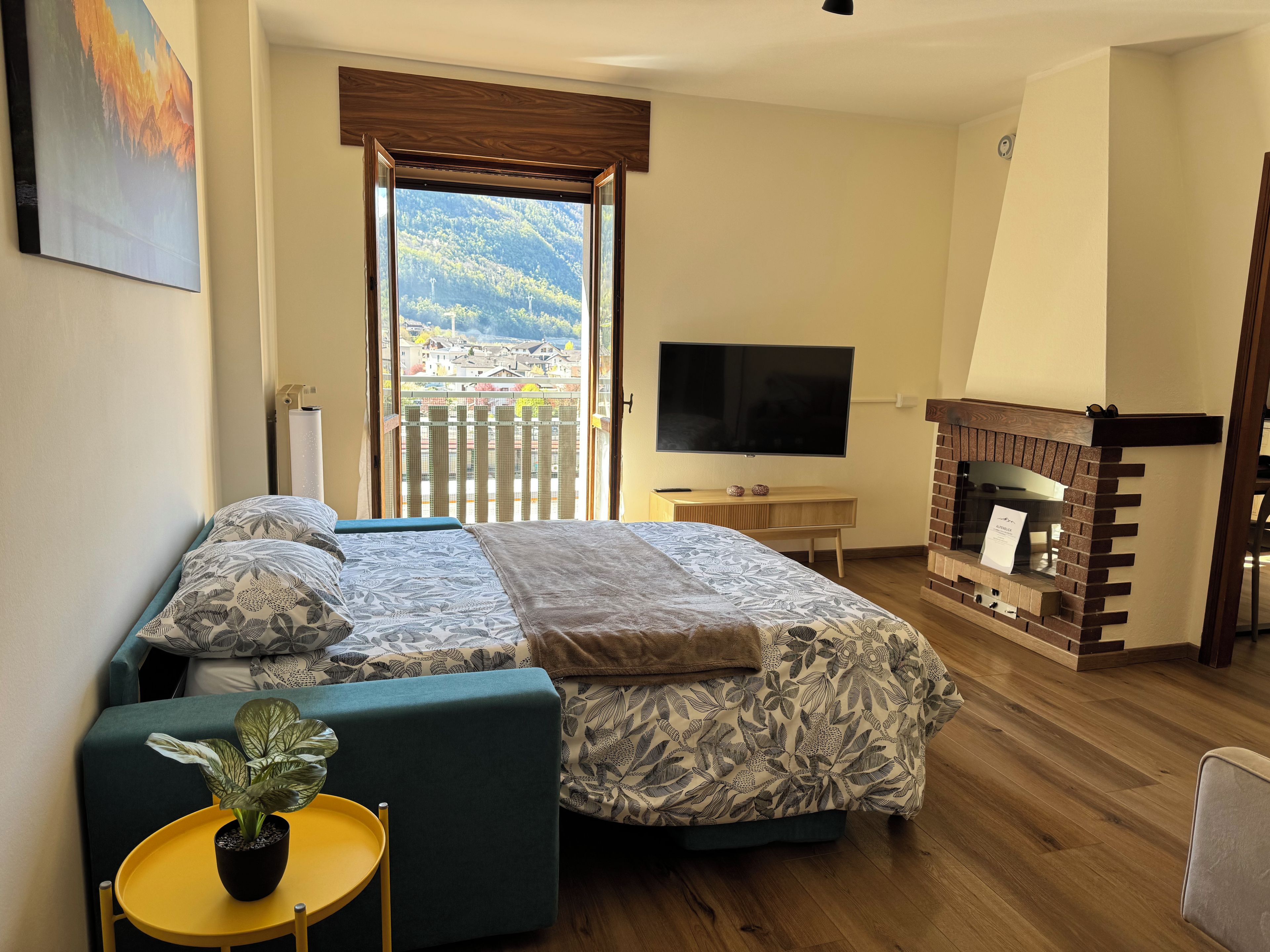Ein Schlafzimmer mit Bett, Fernseher, Kamin und einem Balkon mit Bergblick.