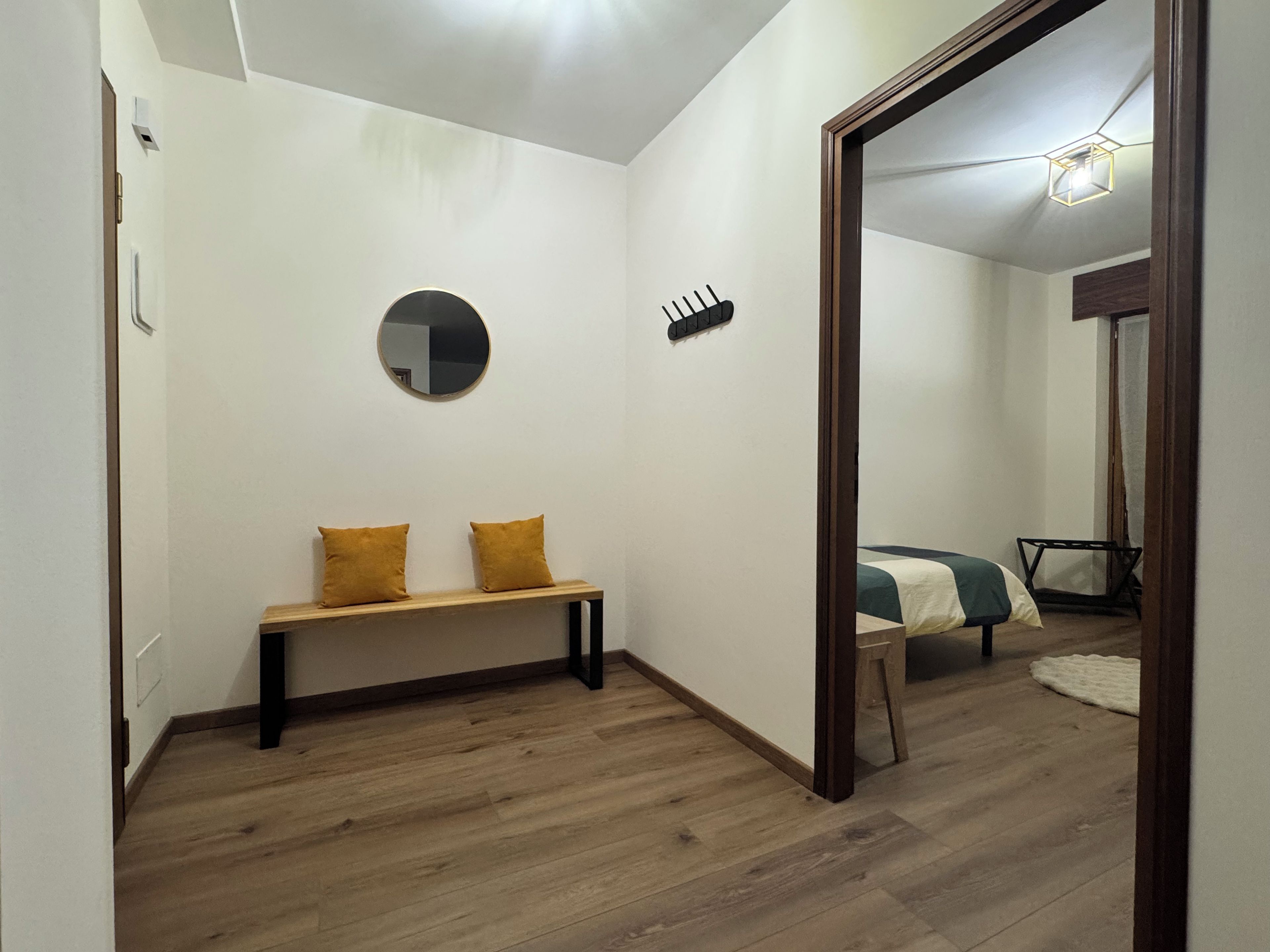 A room with a wooden bench, a round mirror, and a bed with a green and white bedspread.