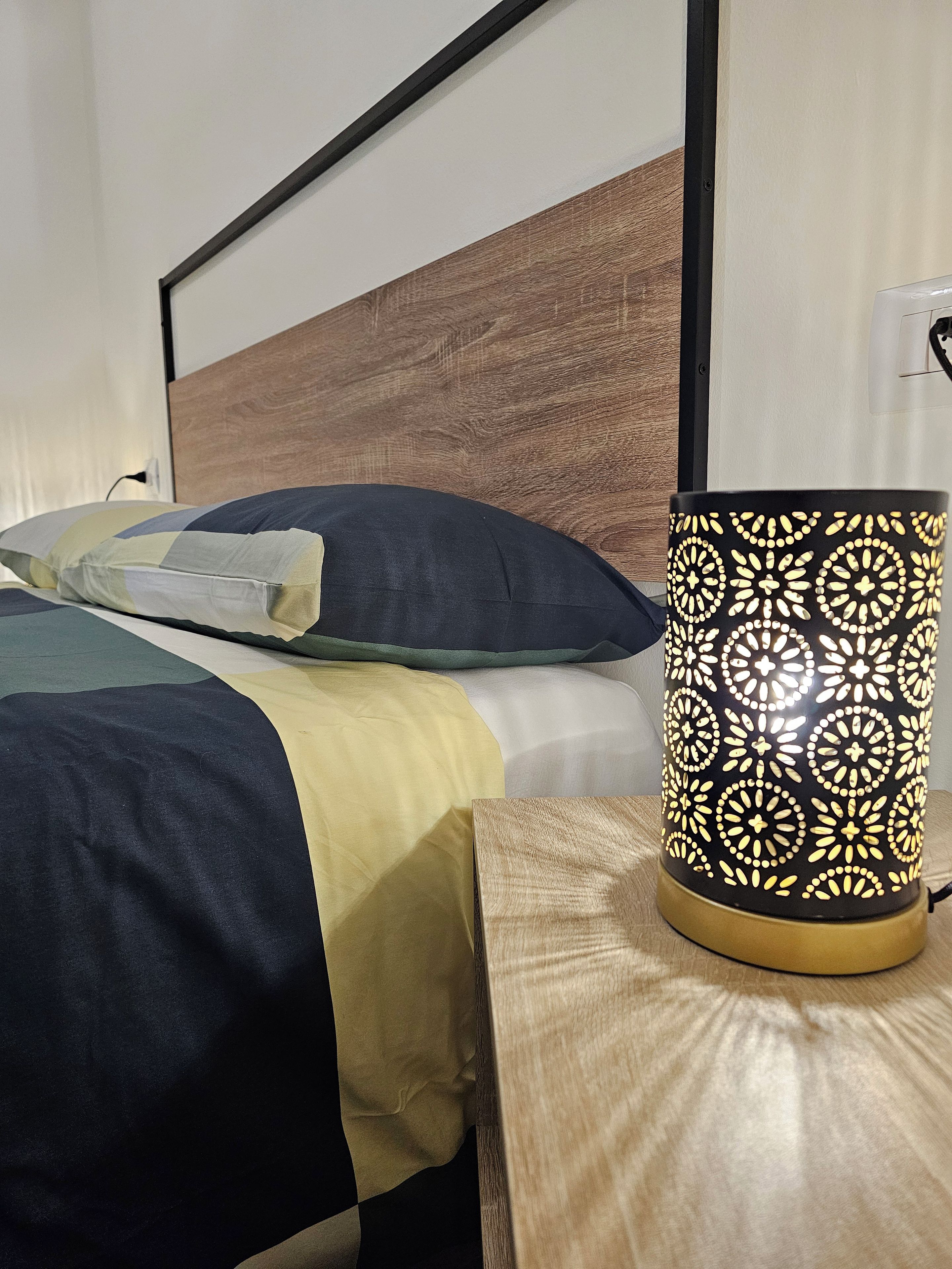 Uma cama com cabeceira de madeira, um abajur com padrão decorativo e uma mesinha de cabeceira.