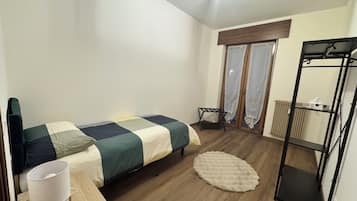 A bedroom with a bed, a bedside table, a lamp, a radiator, and a window with curtains.