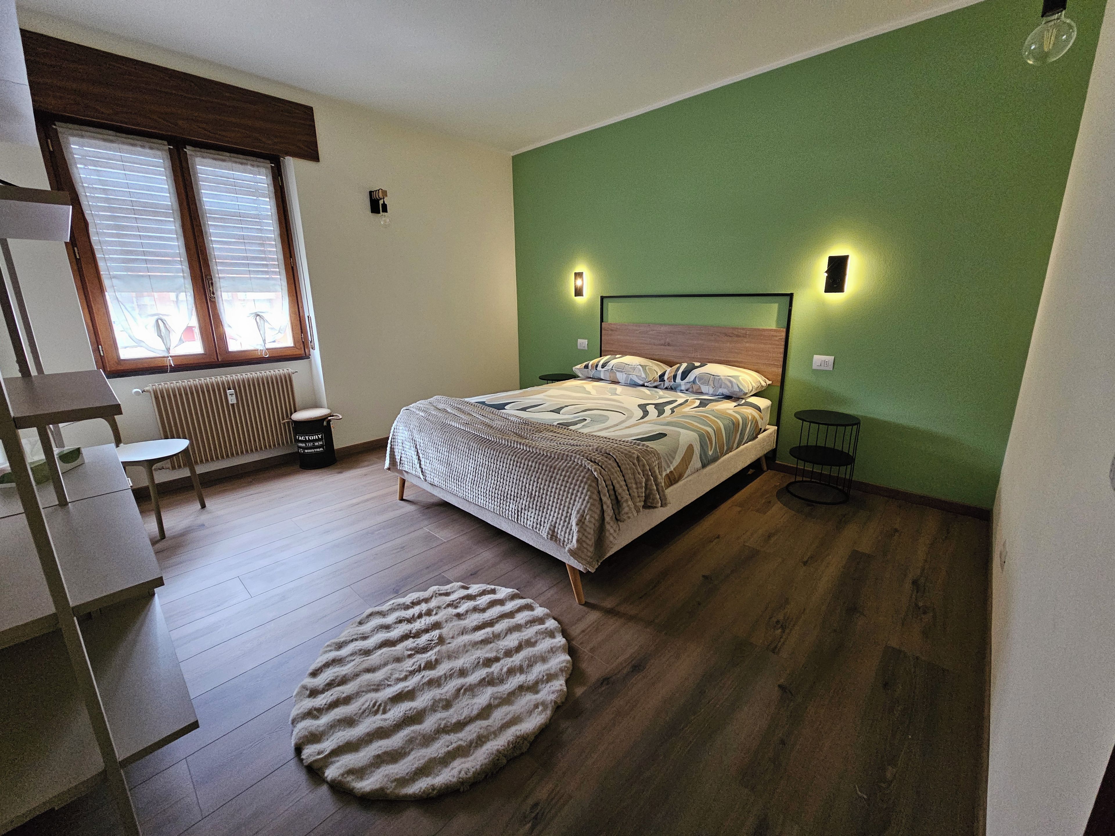 A bedroom with a bed, a round rug, a small table, and a chair.