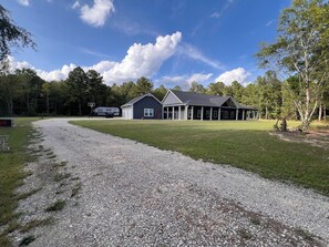 A two-story house with a gravel driveway, a covered porch, and a basketball hoop. - Luxury 10-Acre Southern Estate: Perfect for Tournament Groups two living rooms (Wrens)