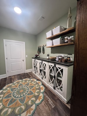 A hallway with a patterned rug, a white door, and a kitchen area with cabinets and shelves. - Luxury 10-Acre Southern Estate: Perfect for Tournament Groups two living rooms (Wrens)