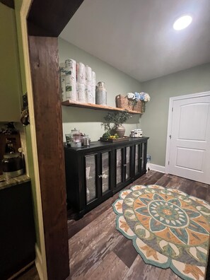A hallway with a patterned rug, a wooden cabinet with glass doors, and a shelf with various items including a vase with flowers.