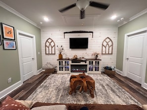 A living room with a fireplace, wooden entertainment center, and a ceiling fan. - Luxury 10-Acre Southern Estate: Perfect for Tournament Groups two living rooms (Wrens)