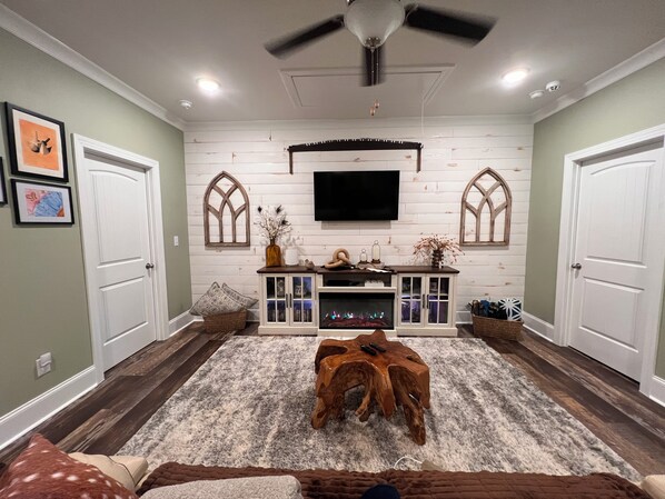 A living room with a fireplace, wooden entertainment center, and a ceiling fan.