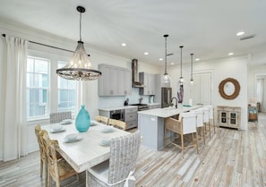 A spacious kitchen with a central island, pendant lighting, and a dining area with a table set for four. - Crisp Ocean Breeze (Santa Rosa Beach)