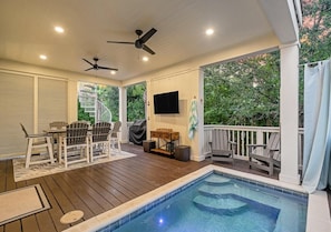 A covered outdoor area with a pool, seating, and a television. - Crisp Ocean Breeze (Santa Rosa Beach)