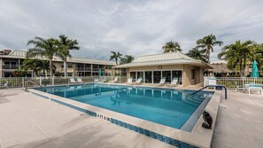A swimming pool with lounge chairs and a small building, surrounded by palm trees. - Coastal Paradise condo close to public beach (Marco island)