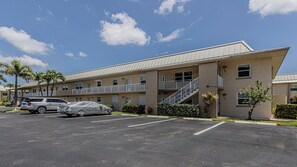 A multi-story hotel with a parking lot, covered cars, and a clear sky. - Coastal Paradise condo close to public beach (Marco island)