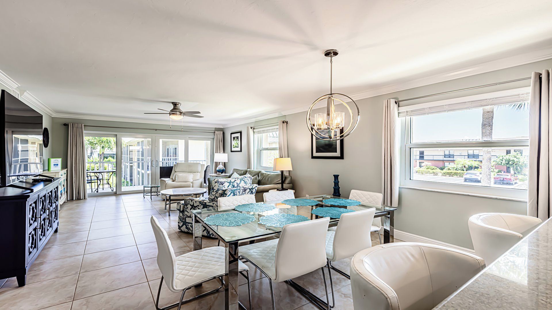 A spacious living area with a dining table, comfortable seating, a ceiling fan, and a view through large windows.