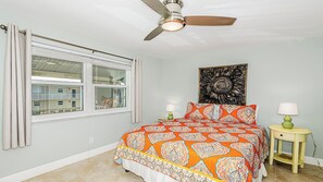 A bedroom with a bed, a ceiling fan, a window with curtains, a wall-mounted artwork, and bedside tables with lamps. - Coastal Paradise condo close to public beach (Marco island)