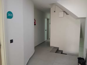 A hallway with a staircase, a fire extinguisher, and a number sign on the wall. - Classic Mannat SRD (Varanasi)
