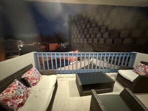Un balcon offrant une vue sur le paysage urbain nocturne, aménagé avec un canapé, une table basse et une rambarde.
