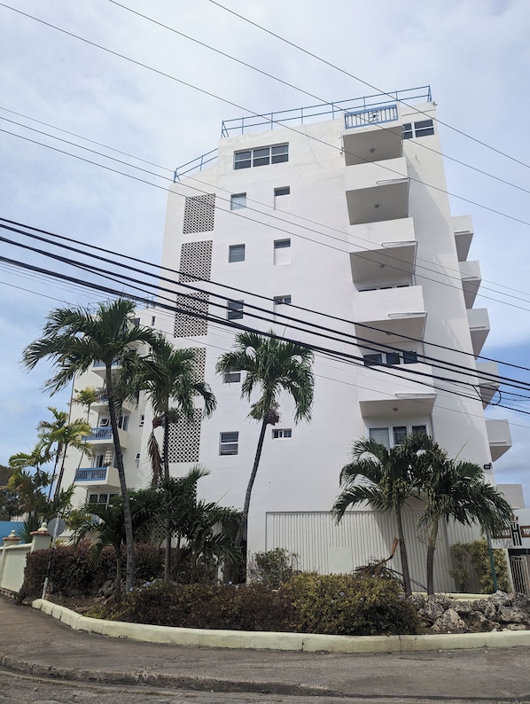 Um edifício com várias andares e varandas, rodeado por palmeiras e um espaço pavimentado.