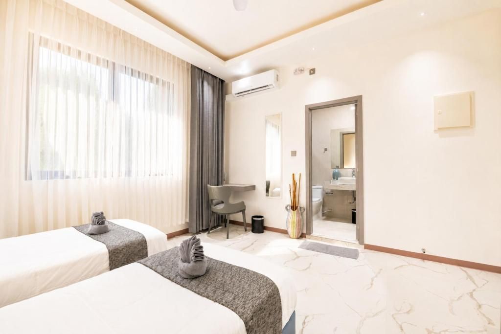 A hotel room with two beds, a desk, a chair, and a bathroom visible through an open door.
