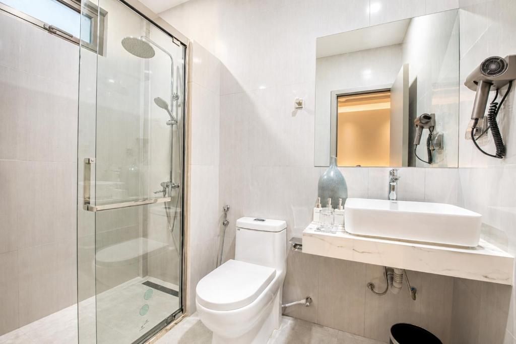 Un baño moderno con ducha envuelta en vidrio, inodoro blanco, lavamanos con espejo y secador de pelo fijado en la pared.