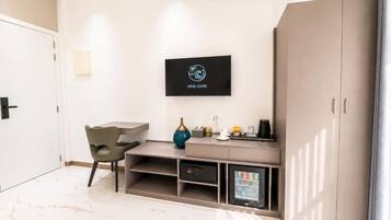 A modern hotel room with a bed, a desk, a chair, a wardrobe, and a television mounted on the wall.