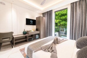 Habitación de hotel con cama, escritorio, televisor y vistas a zonas verdes.