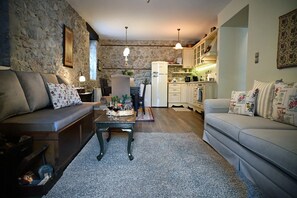 Una sala de estar acogedora con una pared de piedra, un sofá, una mesa de centro con bebidas y una cocina al fondo.