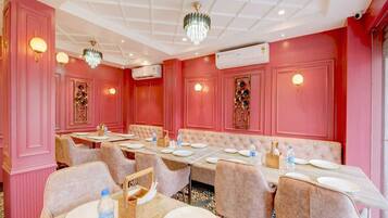 Un comedor con paredes rosadas, candelabros y una disposición central de asientos.