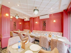 A dining area with pink walls, chandeliers, and a central seating arrangement. - Super Deluxe Room Hotel Midtown Inn (Guwahati)