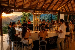 A bar area with a view of mountains, a sign reading 'CHAMANICA', and people socializing.