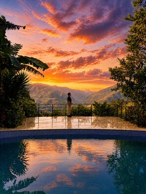 A person standing by a pool with a sunset view of mountains.