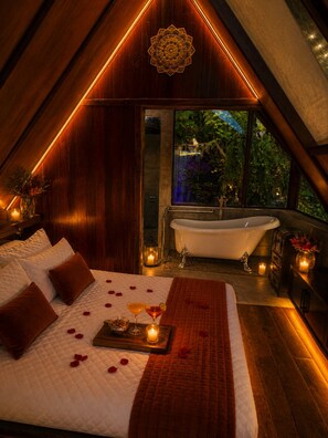 A bedroom with a large bed, a bathtub, and a view of greenery.