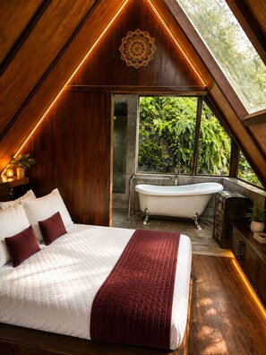 A bedroom with a large bed, a bathtub, and a view of greenery through a window.