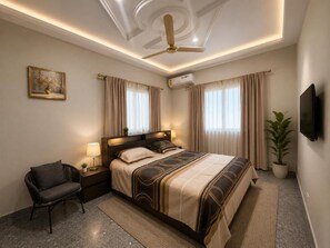 Una habitación de hotel con cama, mesita de noche, lámpara, silla y ventilador de techo.