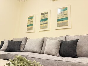 A living room with a grey sofa, three framed artworks on the wall, and a plant in the foreground. - Comfort Stay - Walk Everywhere FJV46O (Manama)