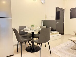 A modern kitchen with a dining table set for four, a refrigerator, and a flat-screen TV mounted on the wall. - Comfort Stay - Walk Everywhere FJV46O (Manama)